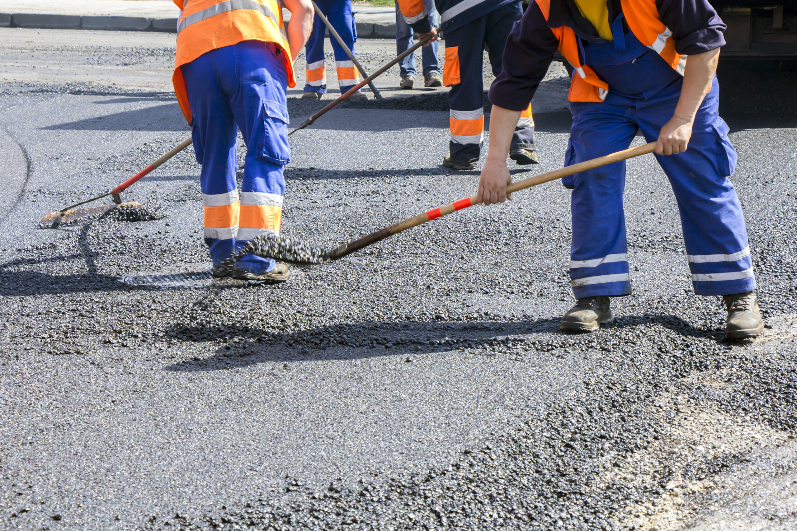 Workers conducting asphalt repair using shovels