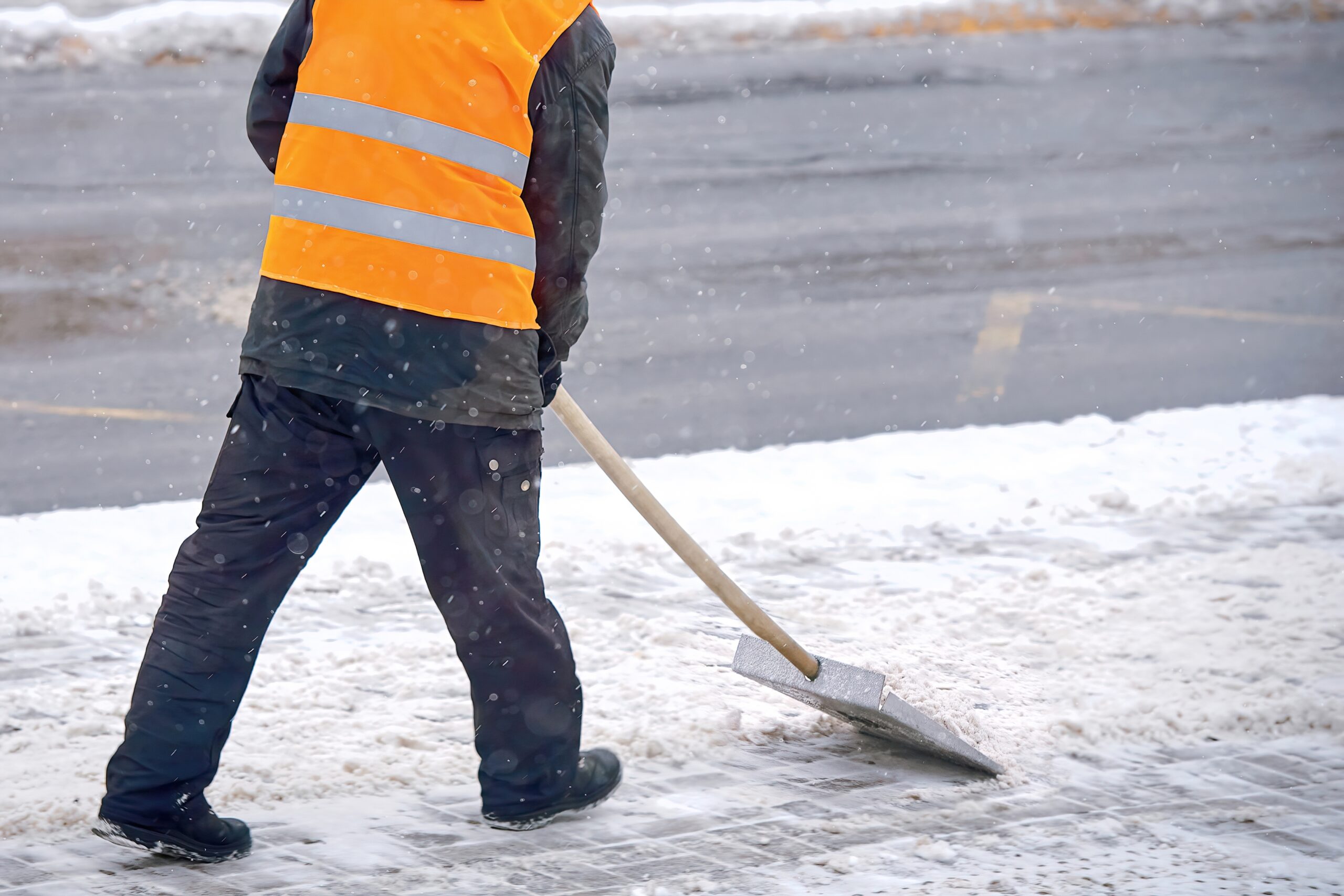 man cleans snow from a pavement sidewalk